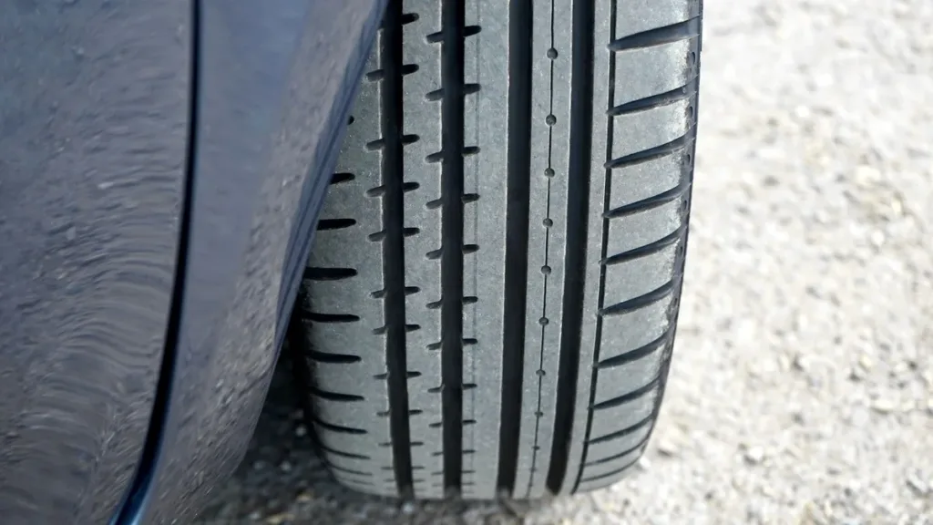 Close-up of a car tyre tread and wheel arch resting on a loose gravel road surface in daylight