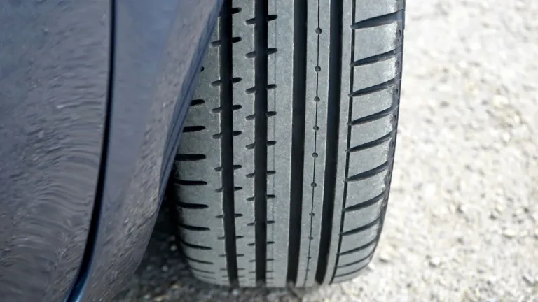 Close-up of a car tyre tread and wheel arch resting on a loose gravel road surface in daylight