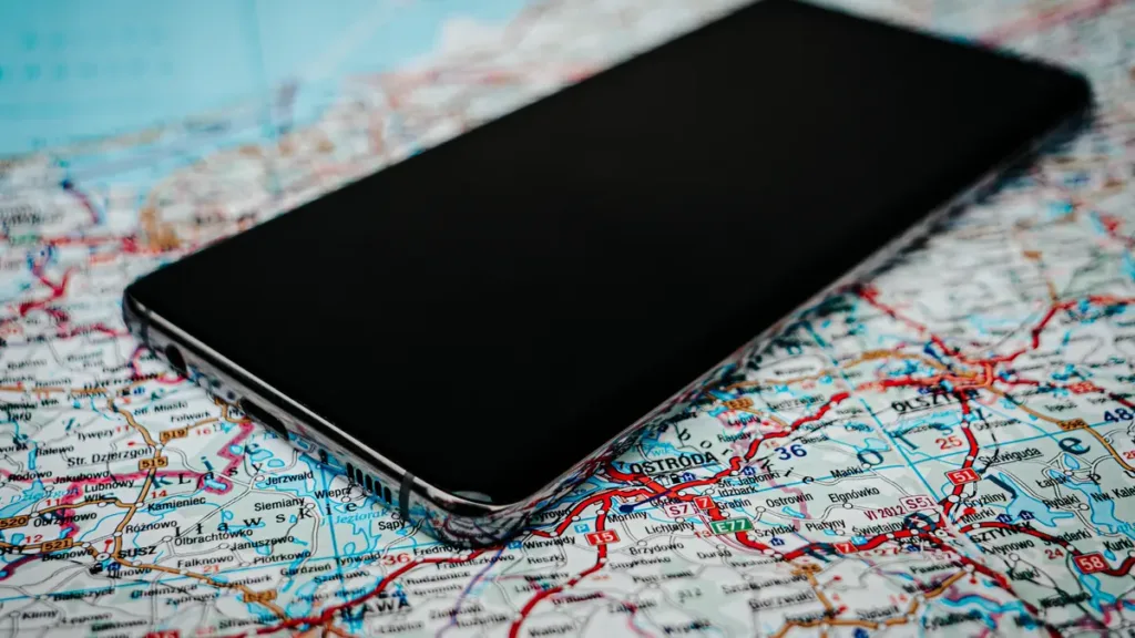 A smartphone with a dark screen lying on a folded paper road map covered in red and blue route lines