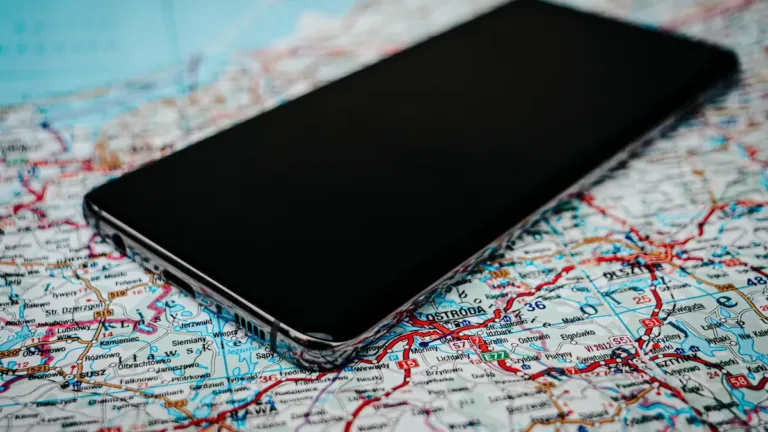 A smartphone with a dark screen lying on a folded paper road map covered in red and blue route lines