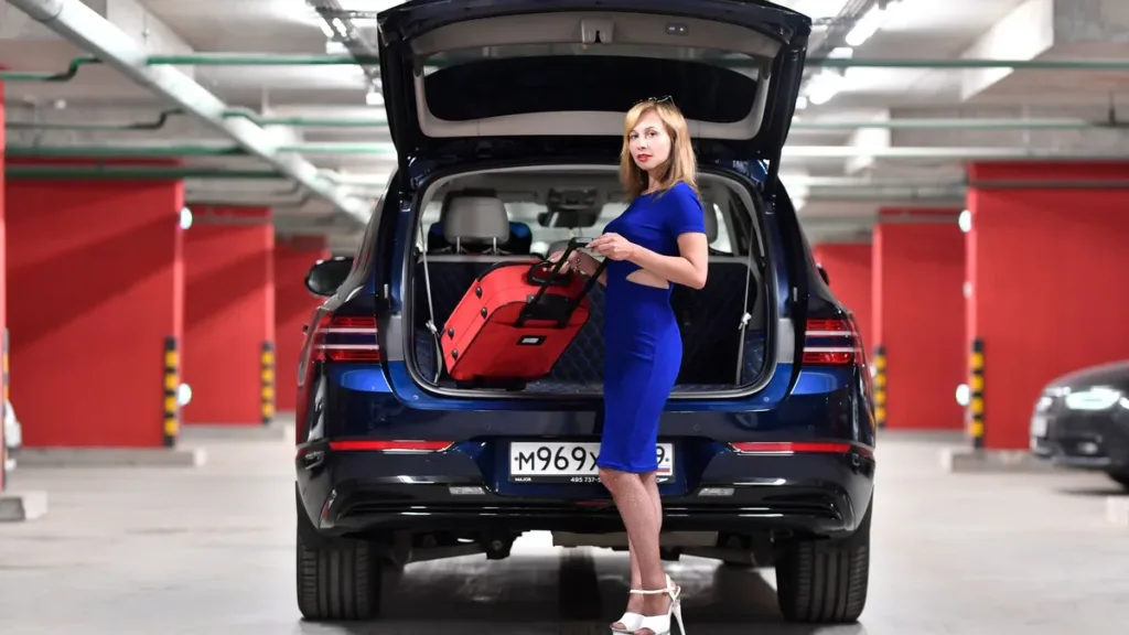 Traveller loading a red suitcase into the open boot of an SUV in a car park
