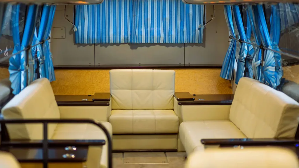 Empty passenger van interior with cream leather lounge seats, a small table and blue pleated window curtains