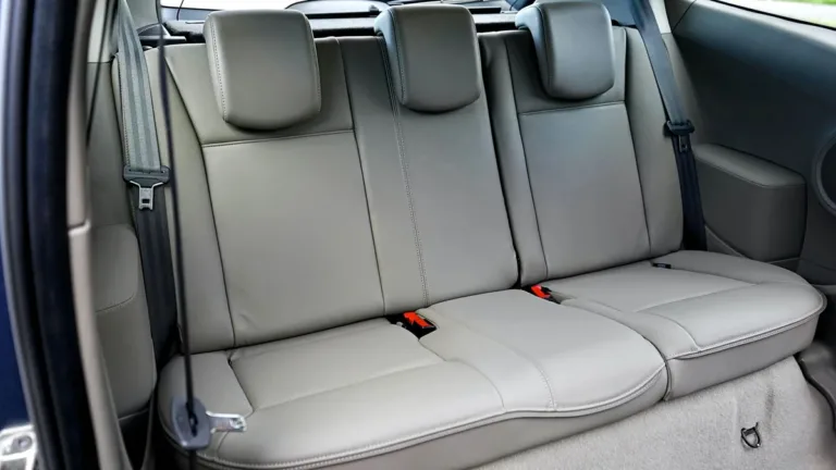 Rear bench seat of a car with grey upholstery, showing three headrests and the rear seat belts and buckles in place