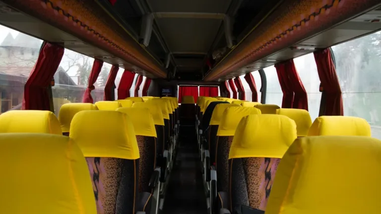 Empty intercity coach interior with rows of yellow-covered seats, red curtains and a central aisle