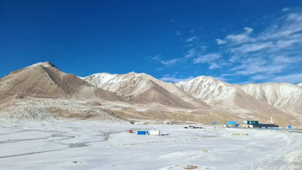 Snow-covered plateau and bare mountains at Khunjerab Pass, with low border buildings under a clear blue sky