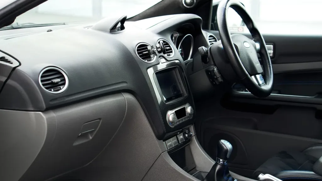 Right-hand-drive car interior seen from the passenger side, showing the steering wheel, dashboard and manual gear lever