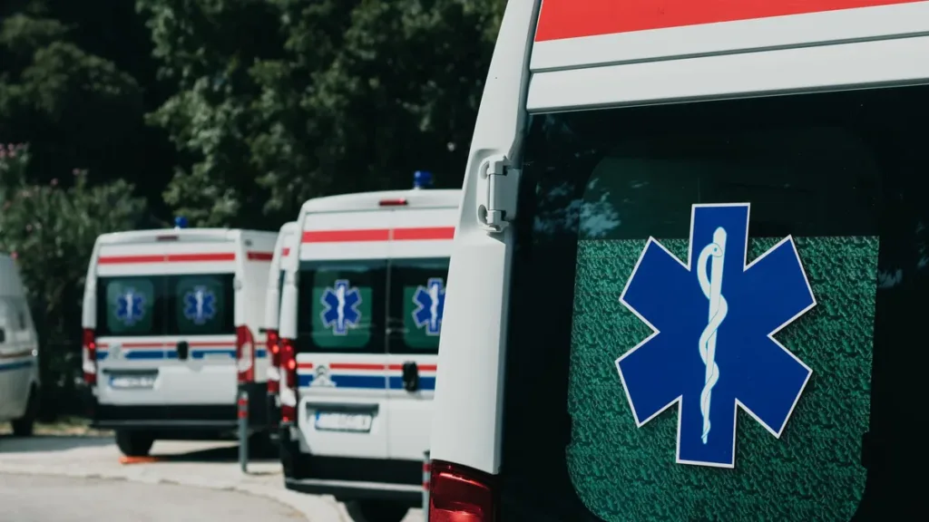 Rear door of a white ambulance with a blue Star of Life emblem, more ambulances parked in a row behind