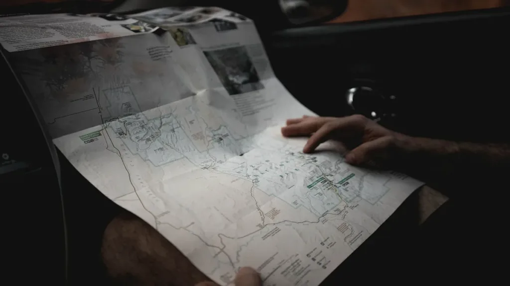 Hands holding an unfolded paper road map inside a car, checking a route before a long journey
