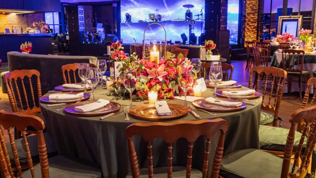 Round banquet table set for an evening event, with a floral centrepiece, candles, plates and wooden chairs