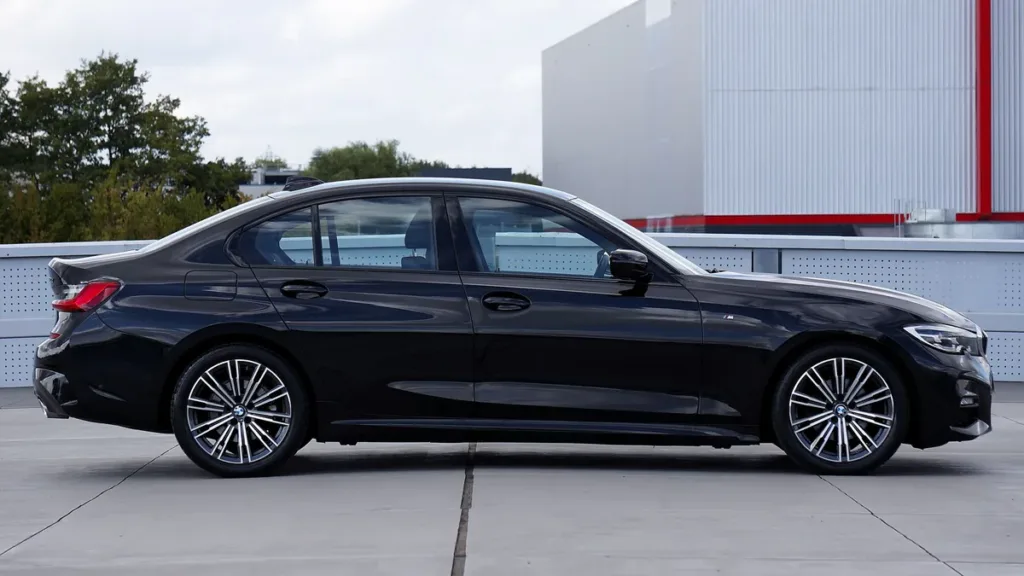 Side view of a black executive saloon car parked on a concrete forecourt beside a modern building