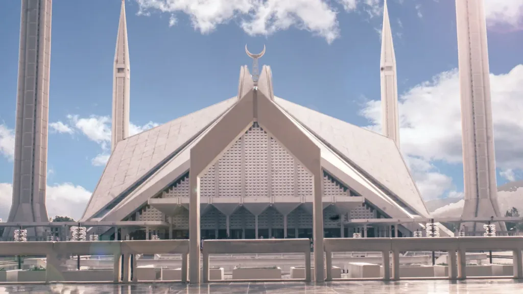 Faisal Mosque in Islamabad with its white minarets and angular roof under a blue sky with scattered clouds