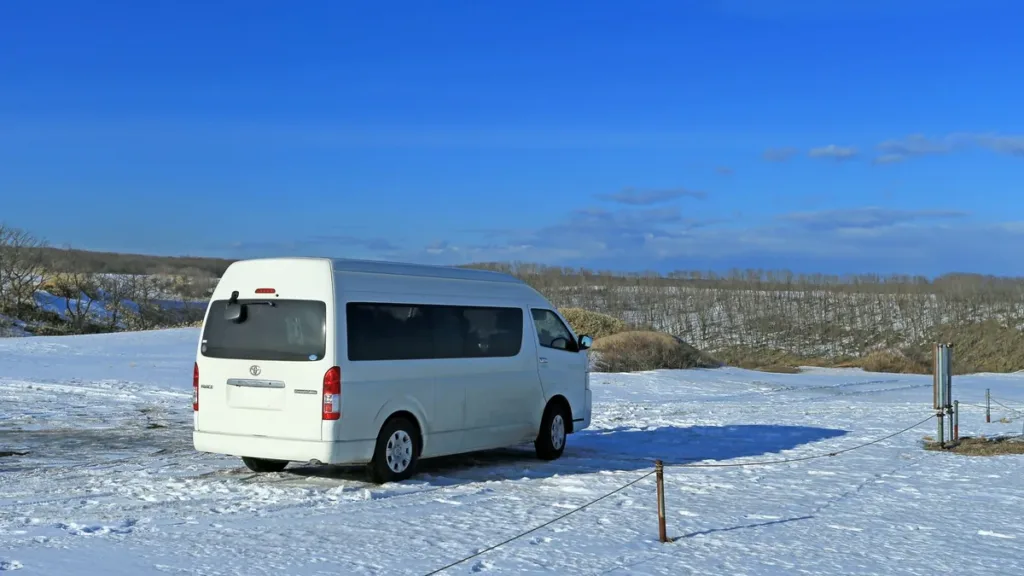 White high-roof Toyota Hiace passenger van parked on a snow-covered field under a clear blue sky