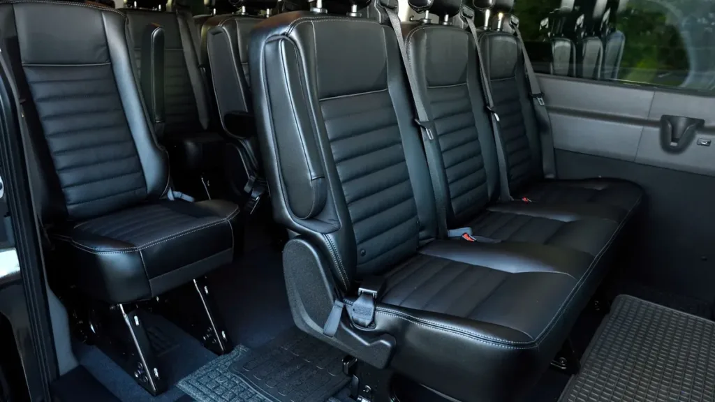Rows of black leather passenger seats with head restraints inside a high-roof van cabin, viewed from the side door