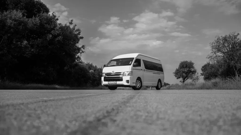 Black and white photo of a white high-roof van on an empty countryside road under cloudy sky