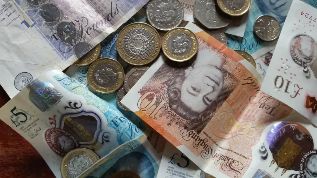 British pound sterling banknotes and coins spread in a close-up pile, the kind of cash visitors pack for a trip