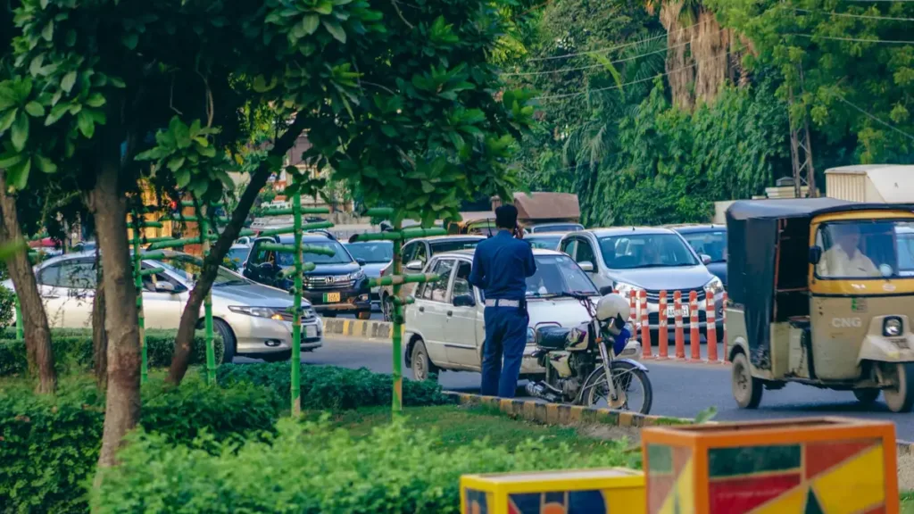 Cars, motorbikes and auto-rickshaws queue in busy Lahore traffic as a policeman directs vehicles beside a green verge