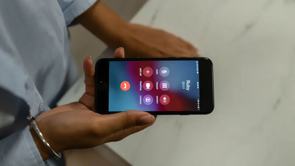 Hands holding a smartphone sideways over a marble table, with an active phone call screen showing