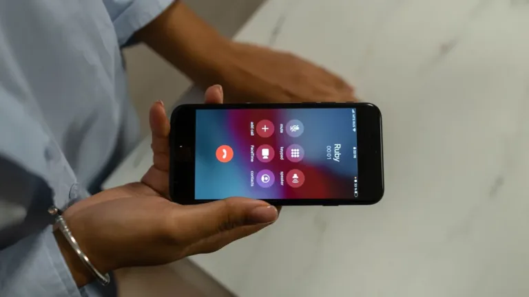 Hands holding a smartphone sideways over a marble table, with an active phone call screen showing