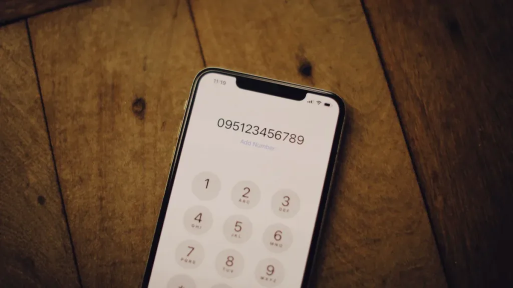 Smartphone lying on a wooden table with its phone dial pad open and a number being keyed in