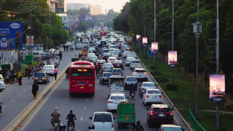 Daytime traffic of cars, buses and motorbikes on a tree-lined city road in Punjab, Pakistan