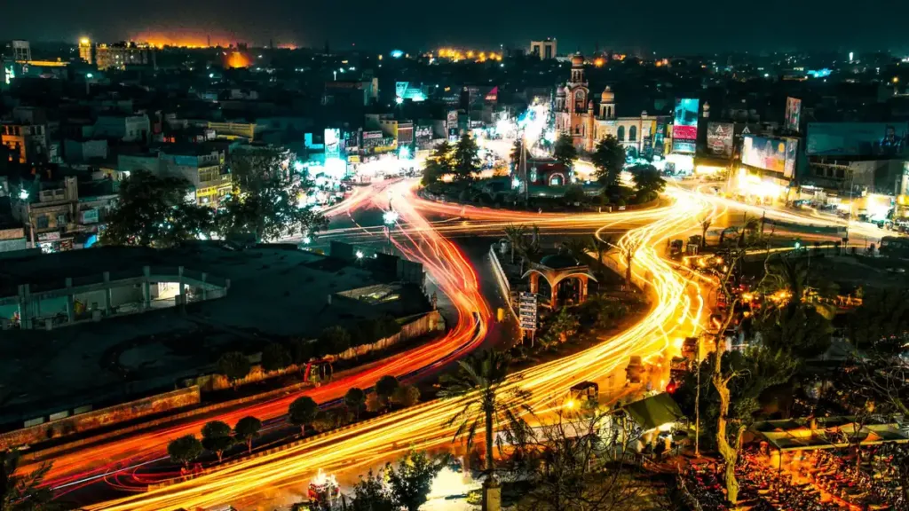 Elevated night view over a city in Pakistan with orange traffic light trails curving through a lit road junction
