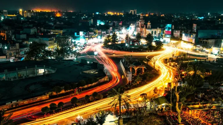 Elevated night view over a city in Pakistan with orange traffic light trails curving through a lit road junction