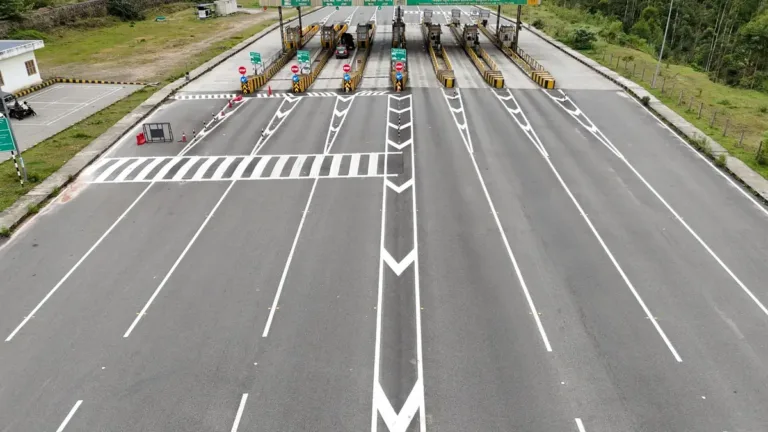 Aerial view of a wide multi-lane highway leading to a toll plaza canopy with booths, set among green hills