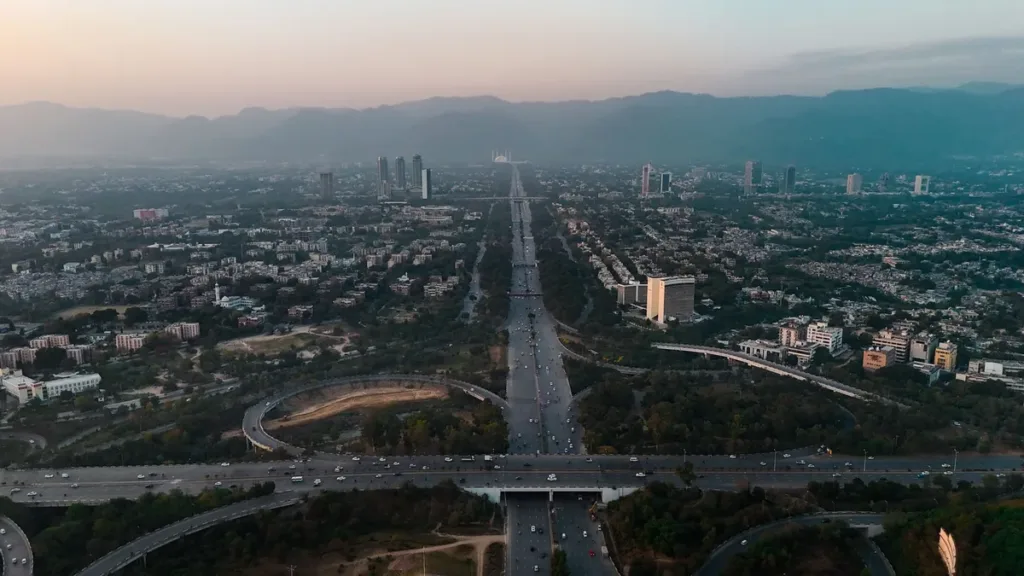 Aerial view of Islamabad at dusk with a wide highway and interchange running through the city toward the Margalla Hills