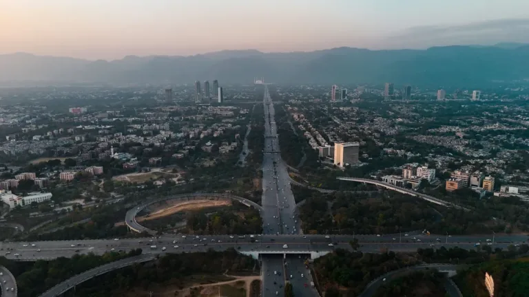 Aerial view of Islamabad at dusk with a wide highway and interchange running through the city toward the Margalla Hills
