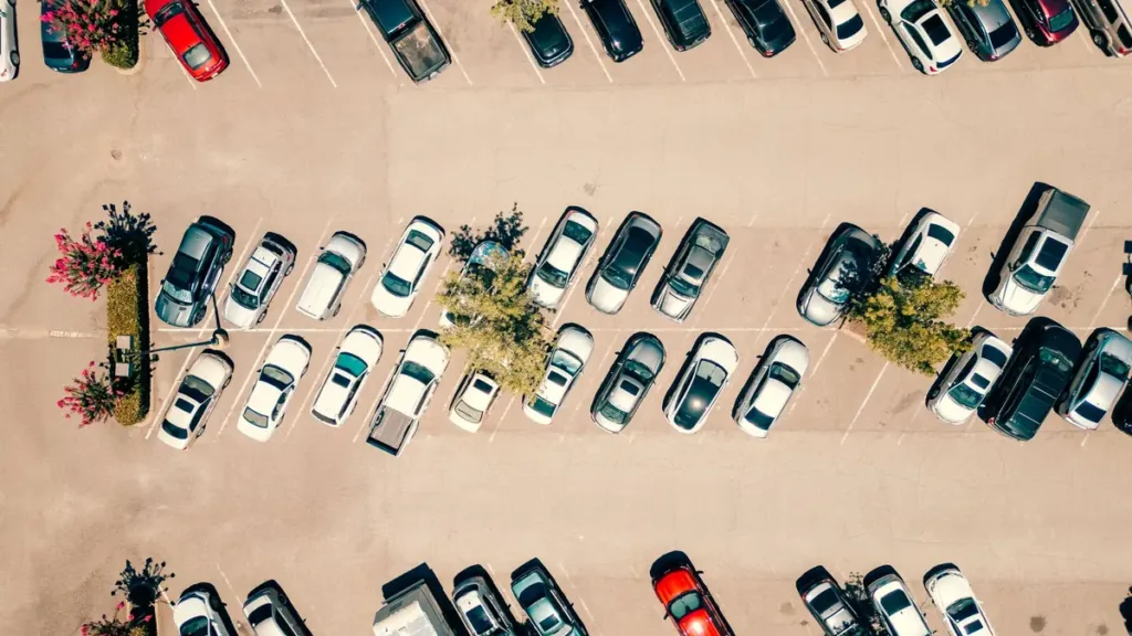 Top-down aerial view of an outdoor car park with rows of parked cars, marked bays and small planted islands