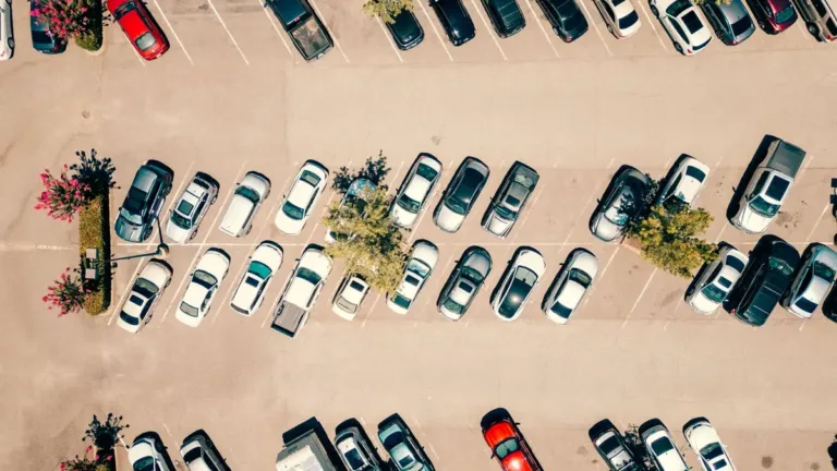 Top-down aerial view of an outdoor car park with rows of parked cars, marked bays and small planted islands