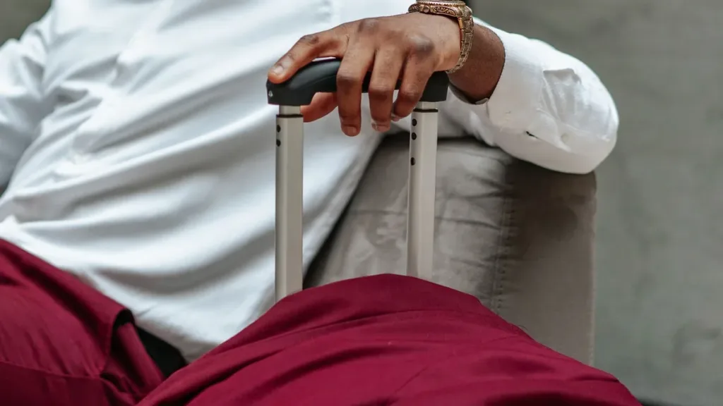 Close-up of a traveller's hand gripping the extended handle of a wheeled suitcase, white shirt and wristwatch