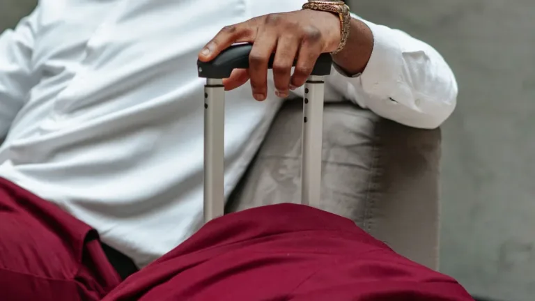 Close-up of a traveller's hand gripping the extended handle of a wheeled suitcase, white shirt and wristwatch