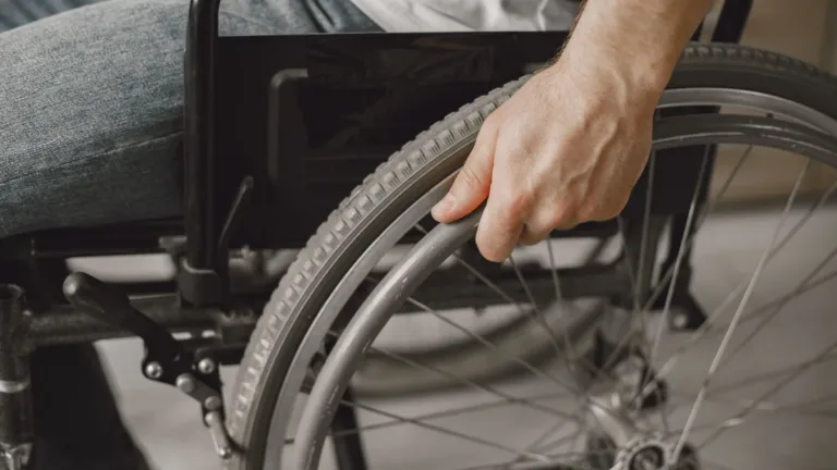 Close-up of a hand gripping the push rim of a manual wheelchair wheel, spokes and tyre in view