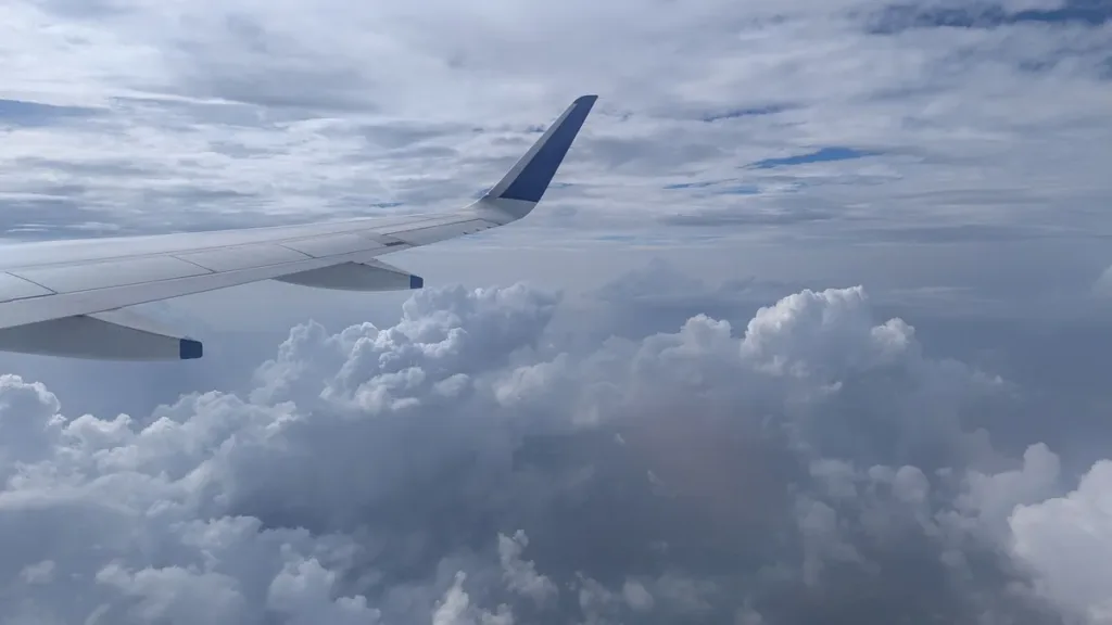 Passenger jet wing seen from a cabin window above a thick layer of grey and white clouds