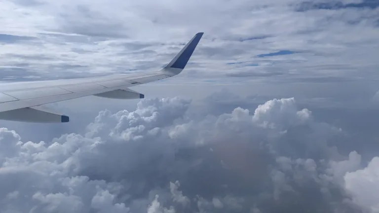 Passenger jet wing seen from a cabin window above a thick layer of grey and white clouds