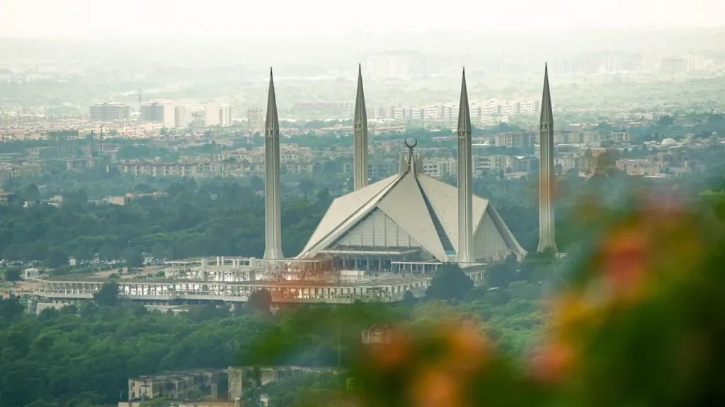 Faisal Mosque's white tent-shaped prayer hall and four minarets above green trees and the hazy Islamabad skyline
