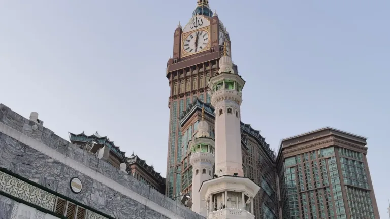 Abraj Al Bait clock tower and hotel towers rising behind a minaret and the stone walls of the Masjid al-Haram