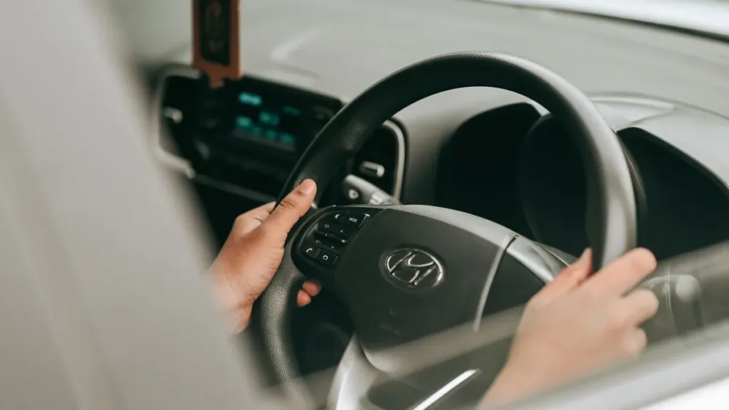 Close-up of a driver's hands on the steering wheel of a right-hand-drive Hyundai car, seen through the side window