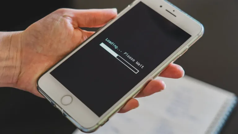 A hand holding a smartphone whose screen shows a loading bar and a please wait message