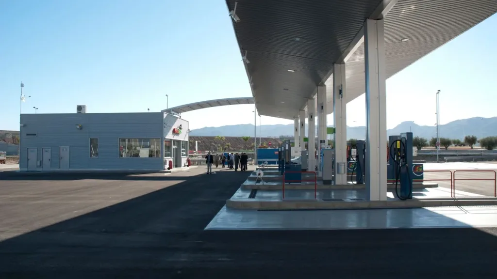 Modern fuel station forecourt with a canopy and pumps under a clear blue sky, low hills on the horizon