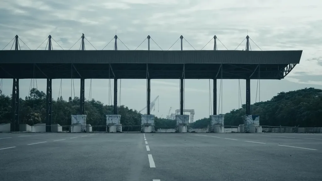 Empty highway toll plaza with a long steel canopy and closed booth lanes under an overcast sky