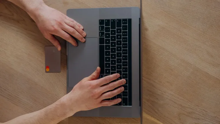 Overhead view of hands typing on a laptop on a wooden desk with a payment card resting beside it
