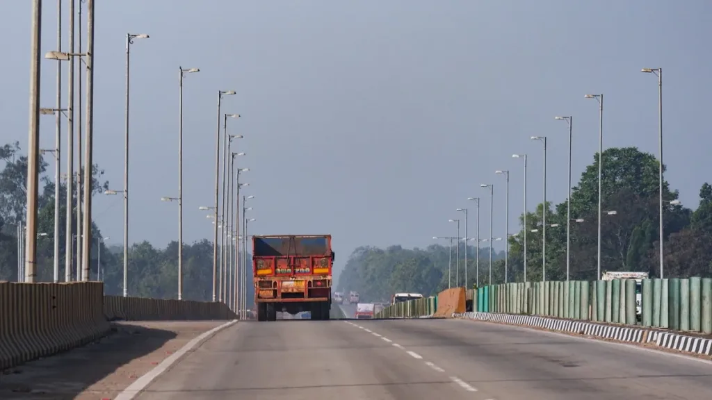 Wide divided highway lined with tall street lamps, an orange cargo truck ahead in the left lane on a clear day