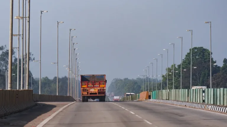 Wide divided highway lined with tall street lamps, an orange cargo truck ahead in the left lane on a clear day