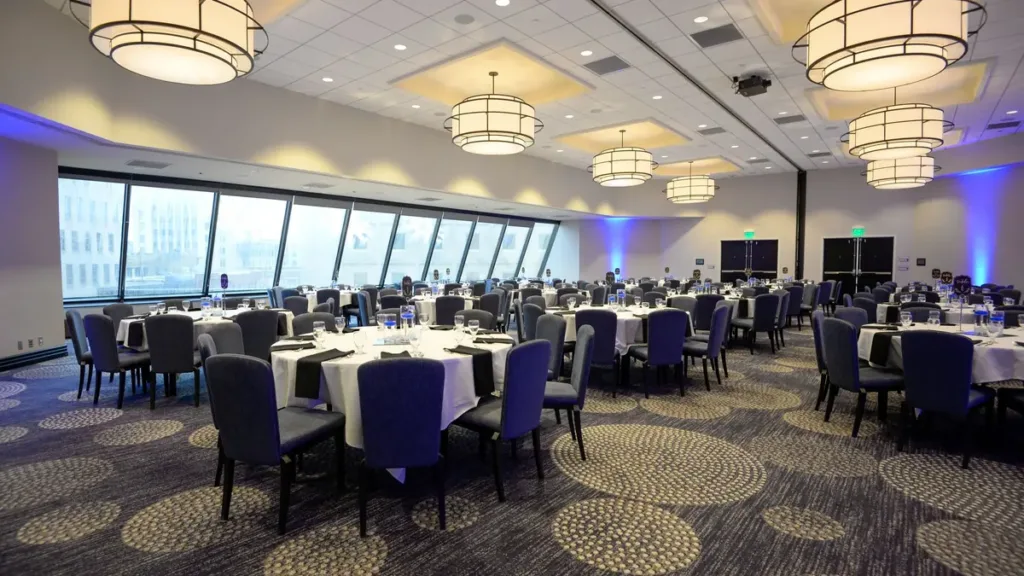 Empty hotel banquet hall set for a formal dinner, round tables with white cloths, navy chairs and pendant lights