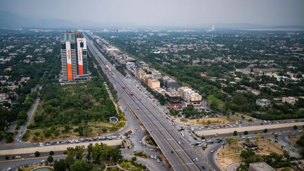 Aerial view of a wide multi-lane expressway running through green city blocks and tall buildings in Islamabad