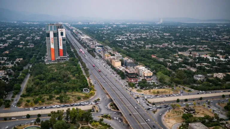 Aerial view of a wide multi-lane expressway running through green city blocks and tall buildings in Islamabad