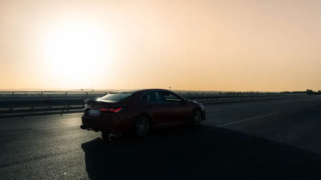 Dark saloon car on an open multi-lane highway at sunset, low sun haze over the road and crash barrier