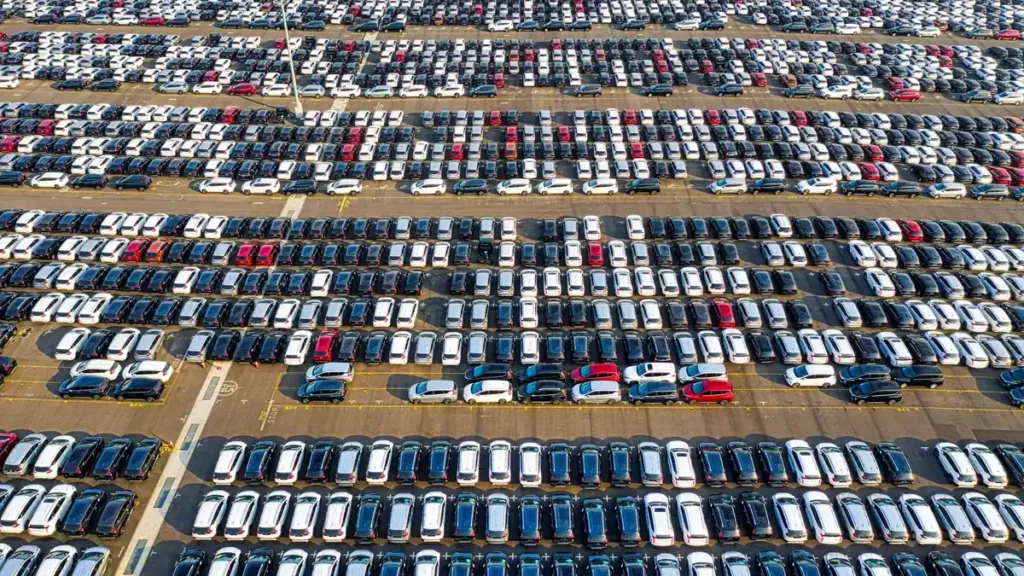 Aerial view of long rows of parked white, silver, blue and dark cars of different sizes on an open lot